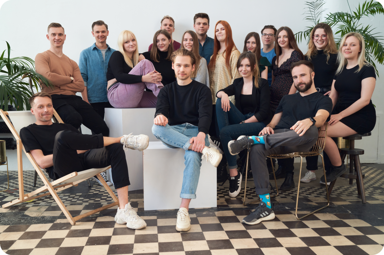 A group of 17 people posing for a photo sitting on chairs or standing on a floor with checked tiles. The team is smiling and facing the camera.