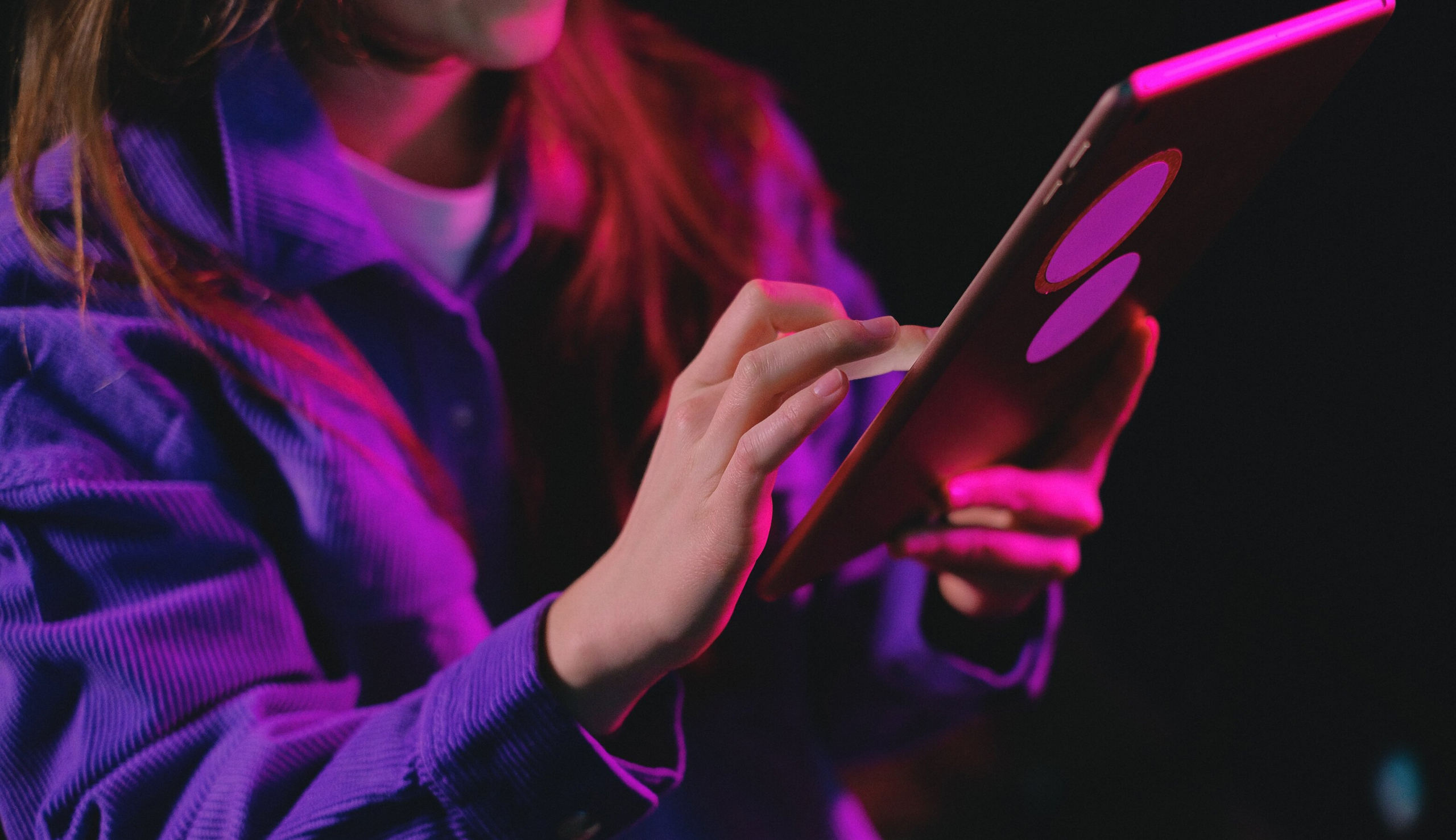 A photo of a person using a tablet. The face of the person is invisible, they have long hair and wear a purple sweater.